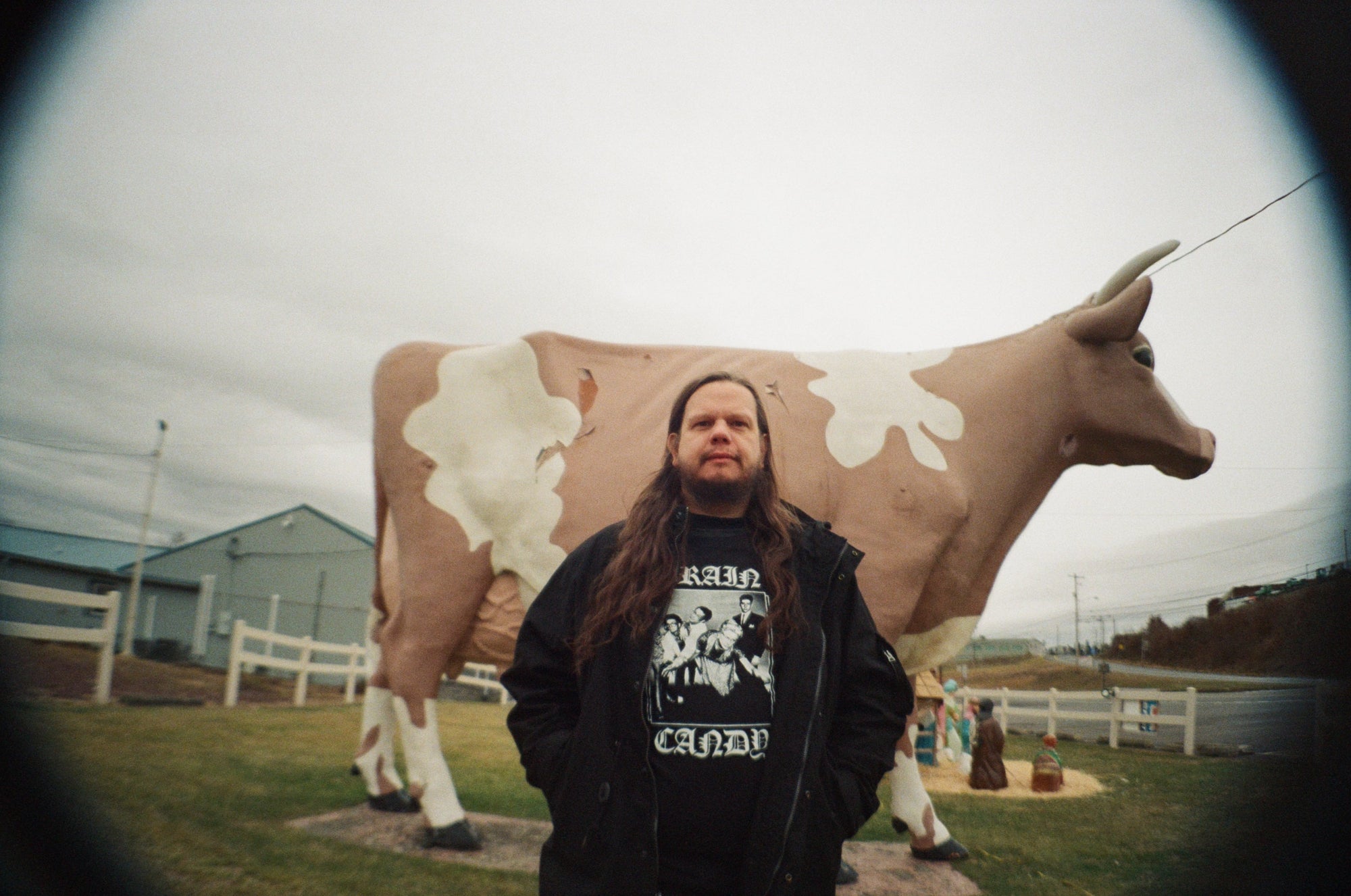 Thom Wasluck of Planning For Burial stands in front of a large, weathered cow statue in an open field.